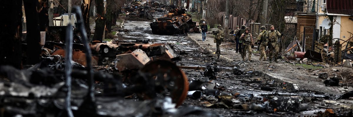 Vojáci prochází kolem zničené ruské techniky ve městě Buča nedaleko Kyjeva