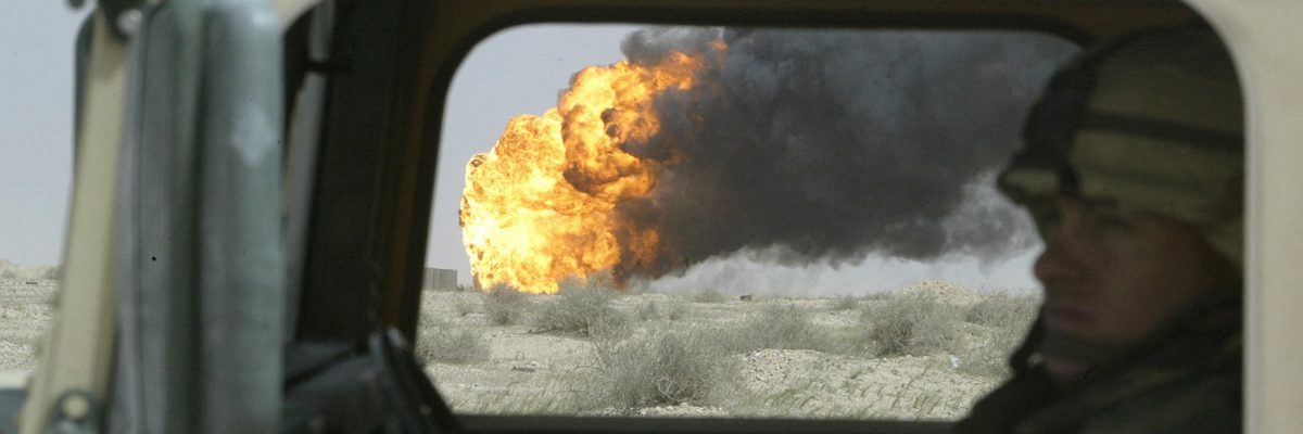 Američtí vojáci projíždí kolem hořícího ropného vrtu, zapáleného ustupující iráckou armádou, 22. března 2003
