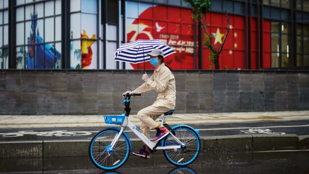 Žena projíždí na sdíleném kole kolem čínské vlajky