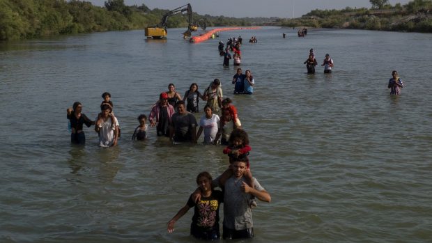 Běženci v řece Rio Grande se brodí kolem bójí, které je mají odradit od překročení hranice mezi USA a Mexikem