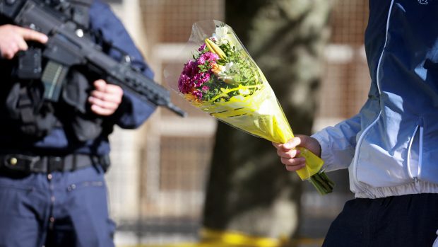 Policisté drží stráž před střední školou Lycee Gambetta-Carnot v Arrasu v severní Francii, zatímco k ní lidé přinášejí květiny, aby uctili památku zavražděného učitele