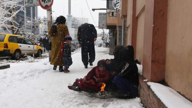 Afghánská rodina se hřeje u ohně na chodníku v Kábulu