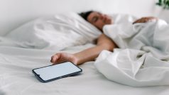 Žena spí v posteli s mobilním telefonem