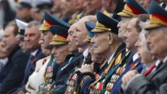 Vladimir Putin sedí mezi veterány a přihlíží vojenské přehlídce.