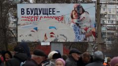 Lidé čekají na distribuci humanitární pomoci s proruským billboardem v pozadí po ústupu ruské armády (ilustrační foto)