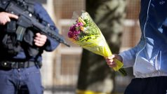 Policisté drží stráž před střední školou Lycee Gambetta-Carnot v Arrasu v severní Francii, zatímco k ní lidé přinášejí květiny, aby uctili památku zavražděného učitele