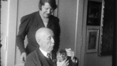 Profesor Janda si ve správní budově zoo hraje s makakem, za ním jeho manželka Ludmila