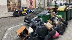 Haldy odpadků jsou předkládané přes sebe, černé pytle se smíšeným odpadem, kartony, krabice, všechno mezi sdílenými koly, auty a před restauracemi