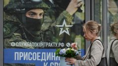 Žena čeká na autobusové zastávce v Moskvě, kde je plakát lákající muže do armády, 25. srpna 2023