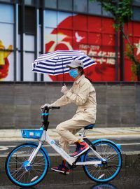 Žena projíždí na sdíleném kole kolem čínské vlajky