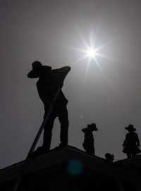 Pokrývači se během vlny veder v texaském městě Eagle Pass kryjí před sluncem klobouky
