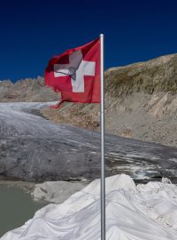 Švýcarská vlajka u vchodu do ledové jeskyně na ledovci Rhone (ilustrační foto)