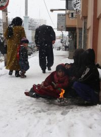 Afghánská rodina se hřeje u ohně na chodníku v Kábulu