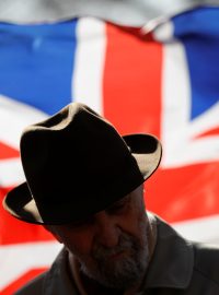Muž stojící před britskou vlajku před budovou parlamentu.