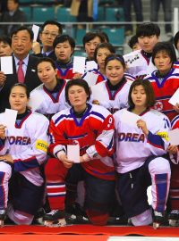 První společný olympijský tým by měly být hokejistky. Na snímku z dubna 2017 spolu pózují jihokorejské (v bílém) a severokorejské (v červeném) hokejistky u příležitosti vzácného společného utkání v jihokorejském Kangnungu. Uprostřed šéf organizačního výboru pro ZOH 2018.
